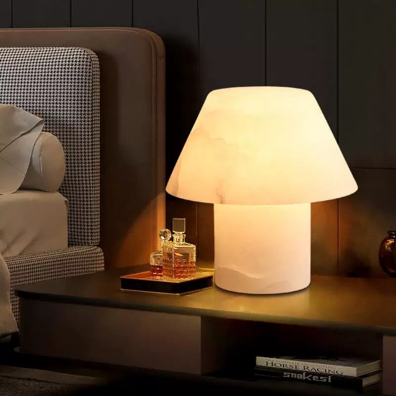 Modern alabaster table lamp with warm ambient glow placed on a bedside table, ideal for bedroom and living room lighting.