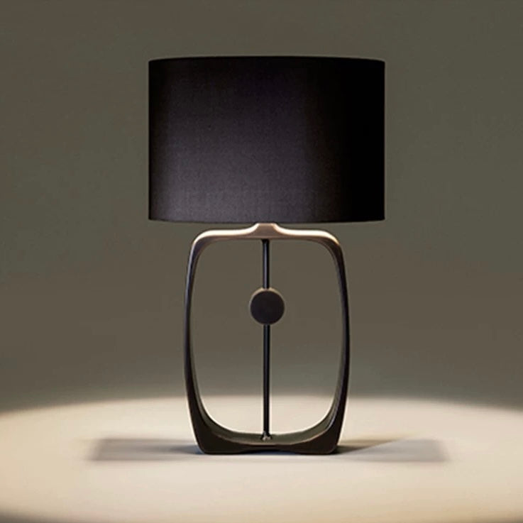 Black frame table lamp with sculptural metal base and fabric shade, providing warm ambient lighting for bedrooms and contemporary interiors.
