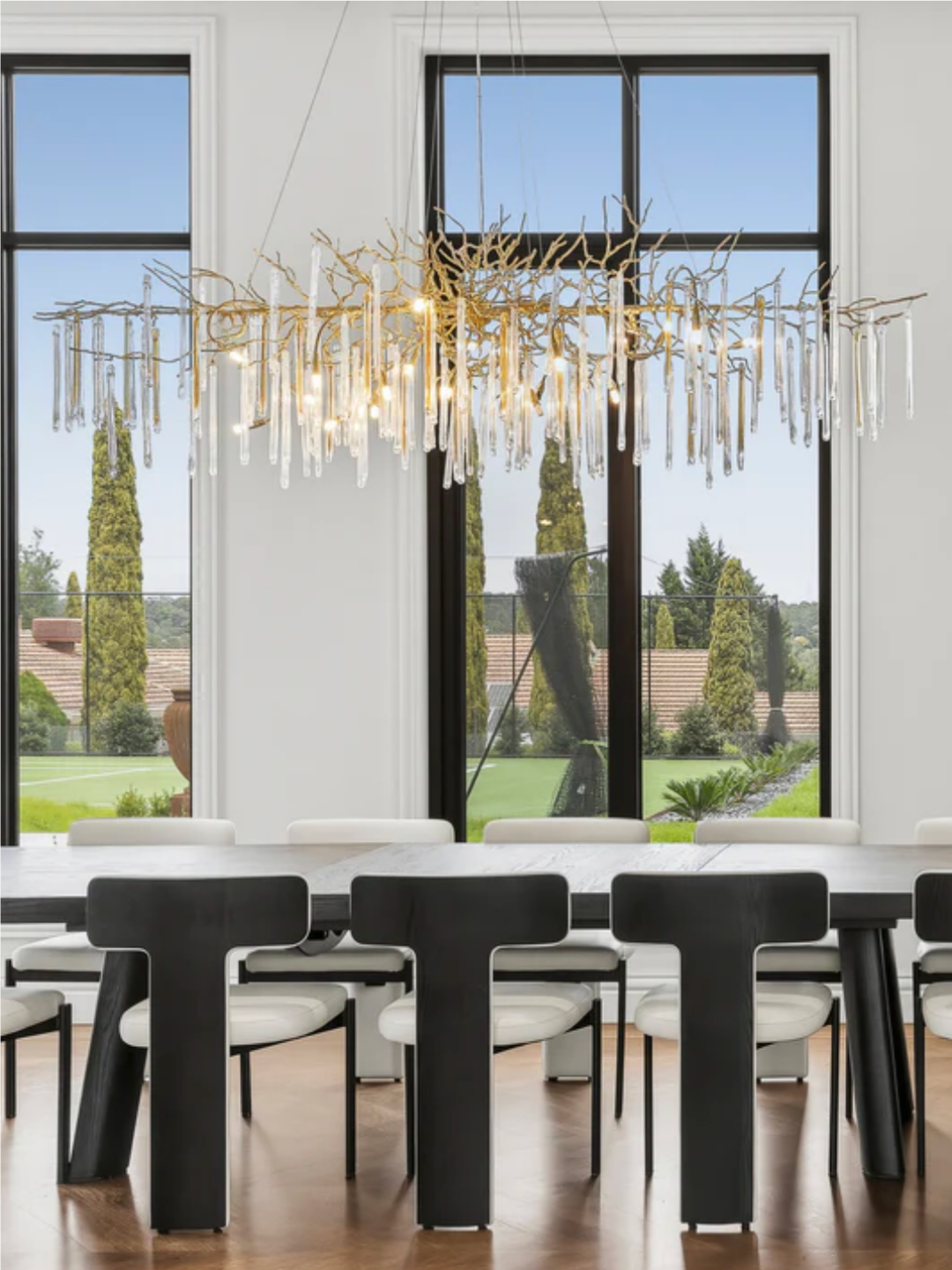 Glazed Icicle Brass Chandelier of brass branches and clear glass icicles above a dining table in a double-height room with garden views