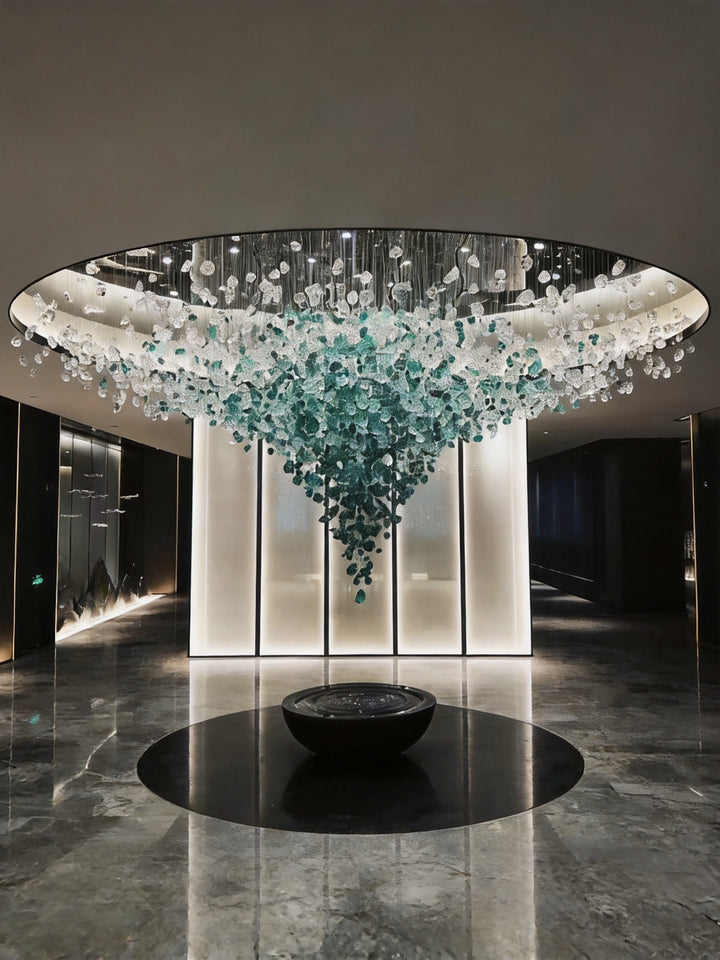 Green and clear hand-blown glass stone sculpture chandelier suspended beneath a circular ceiling in a luxury hotel lobby with black marble flooring, StoneLuxe Sculpture by Lucretia