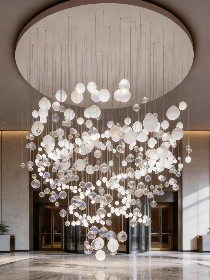 White and clear hand-blown glass bubble chandelier suspended from a circular ceiling in a bright commercial building lobby with marble flooring, BubbleGlow Bespoke Lighting by Lucretia