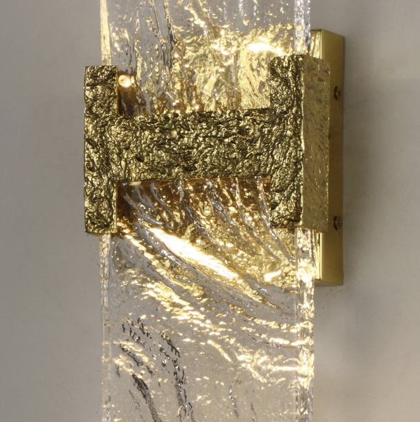 close-up of incu wall lamp showing carved brass fixture and textured glowing glass panel providing soft ambient led illumination for interior spaces