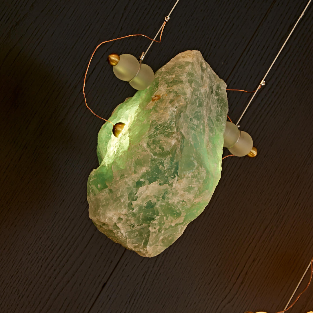 Green natural Brazilian crystal pendant light with sculptural brass frame for luxury architectural interiors.