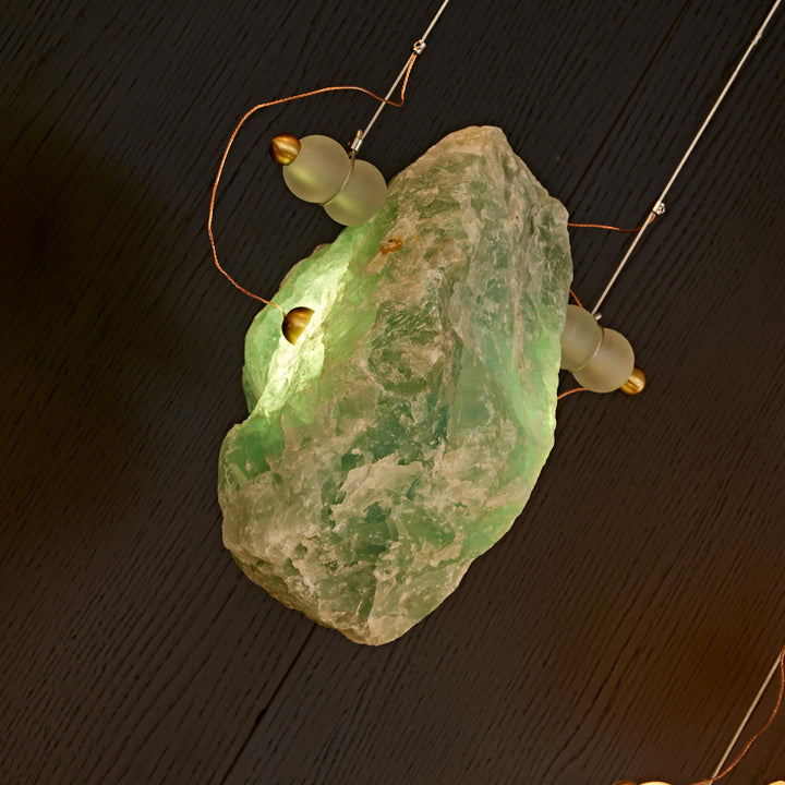 Green natural Brazilian crystal pendant light with sculptural brass frame for luxury architectural interiors.