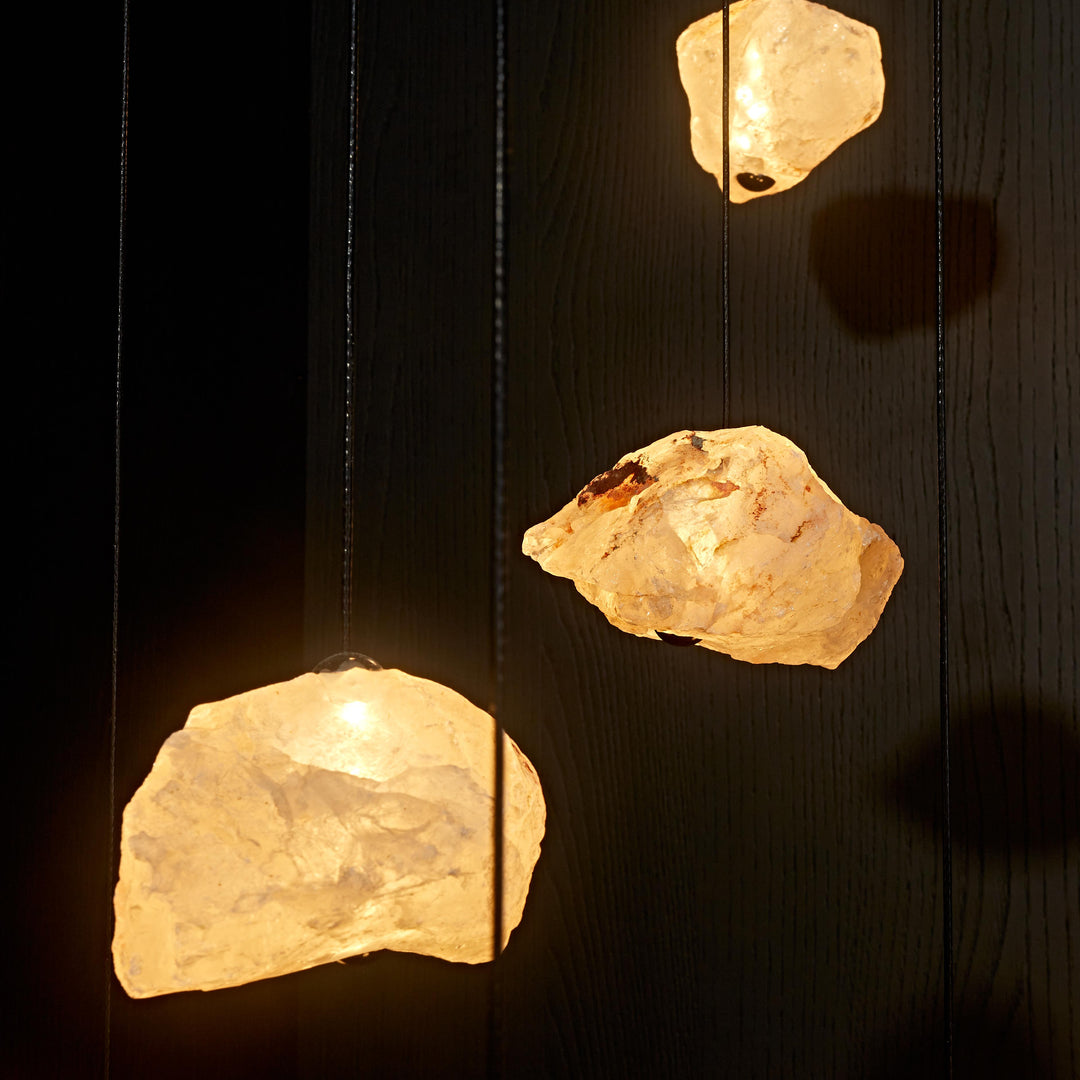 Aether Brazilian Natural Crystal Pendant Lights suspended before a dark stone backdrop, celebrating the natural texture and organic form of raw crystal.