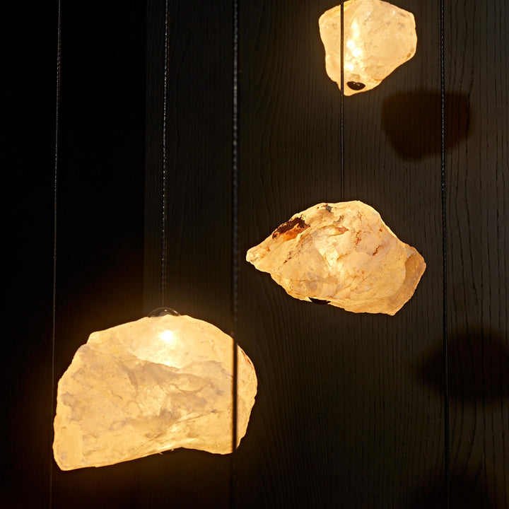 Aether Brazilian Natural Crystal Pendant Lights suspended before a dark stone backdrop, celebrating the natural texture and organic form of raw crystal.