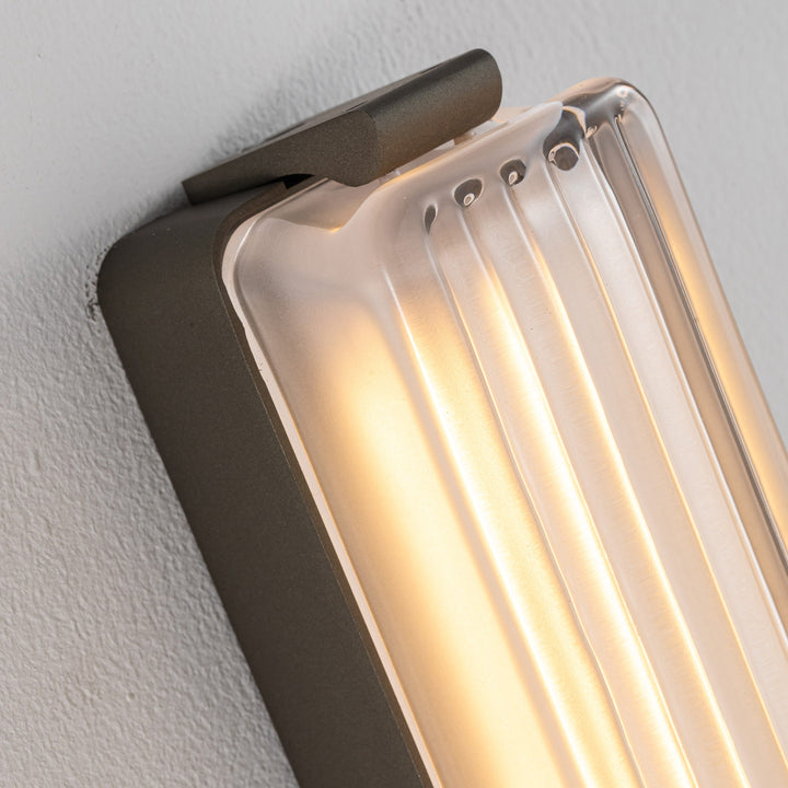 Striato designer wall lamp showing ribbed satin glass detail with soft LED wall light glow suitable for luxury lighting and interior applications.