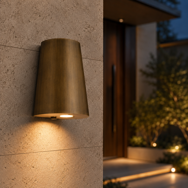 Solid brass tapered outdoor wall light installed on a modern exterior wall with warm architectural LED lighting.