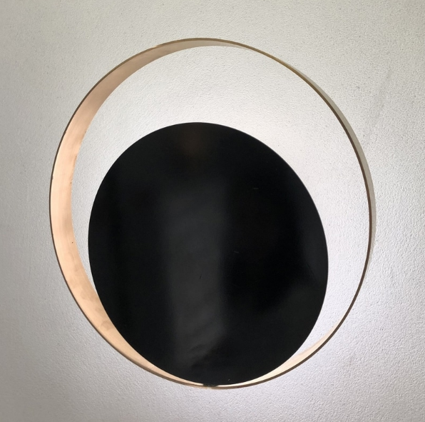 side angle photo of lunar wall lamp displaying round brushed steel frame with soft halo glow and minimalist contemporary wall lighting design