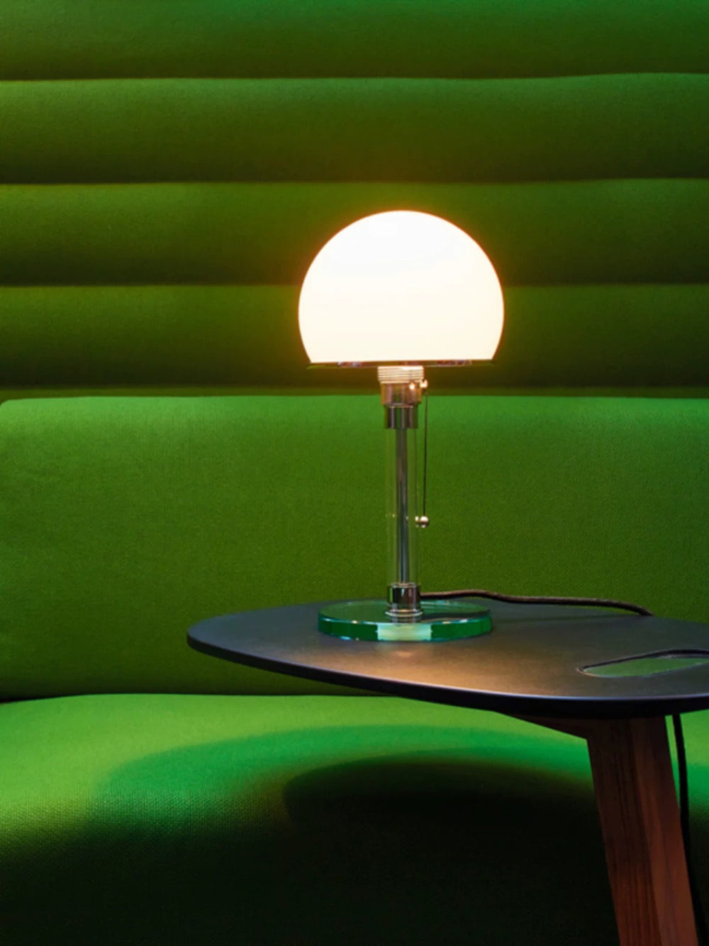 Opal glass table lamp with sleek metal base placed beside a green sofa, ideal for bedside lighting, living rooms and contemporary interiors.