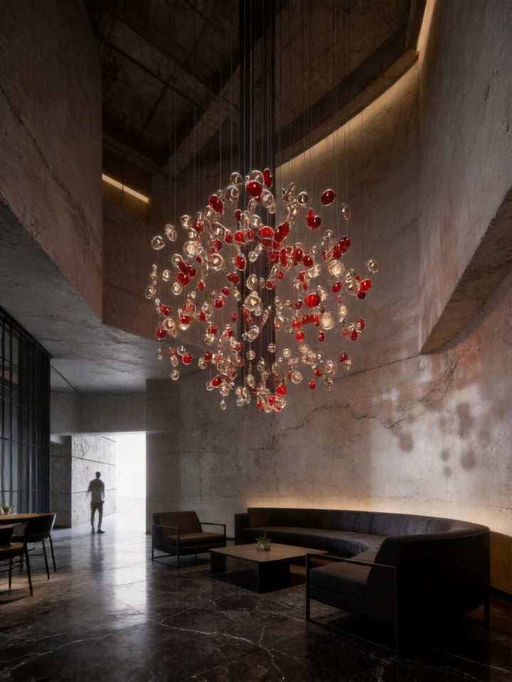 Red and clear hand-blown glass bubble chandelier in a double-height industrial style lobby lounge with concrete walls and curved seating, BubbleGlow Bespoke Lighting by Lucretia