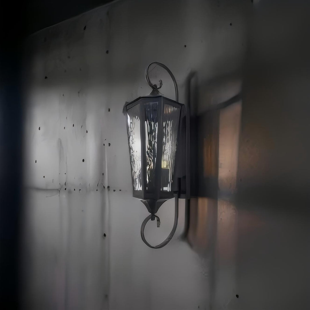 Riviera brass outdoor wall lamp in brushed black casting a soft ambient glow on an exterior wall for garden or veranda lighting.