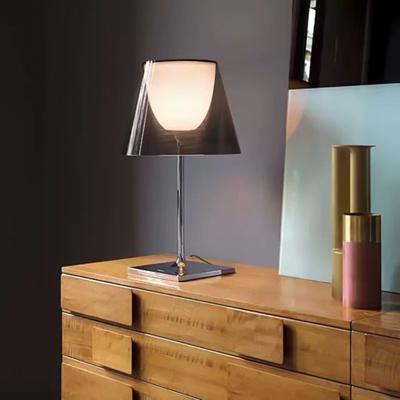 Modern table lamp with smoked grey acrylic shade and warm ambient glow styled on a wooden cabinet, ideal for bedside and living room lighting.