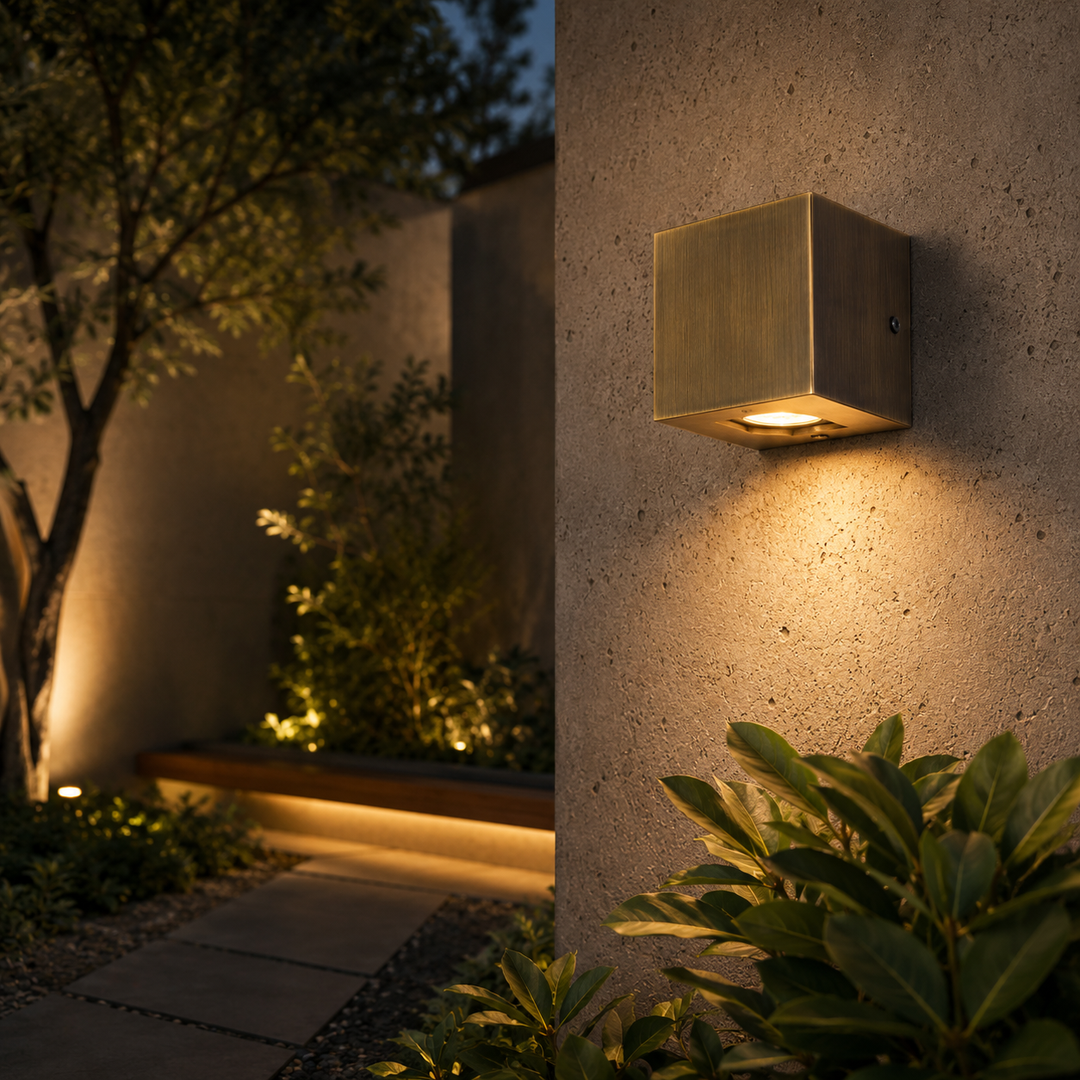 Solid brass bronze wall light installed on a modern architectural exterior wall, providing warm IP65 outdoor lighting for luxury residential landscaping.
