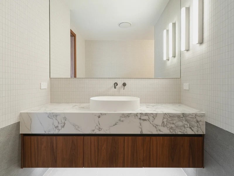 Running Water wall lamps beside the mirror above a marble vanity with a timber cabinet