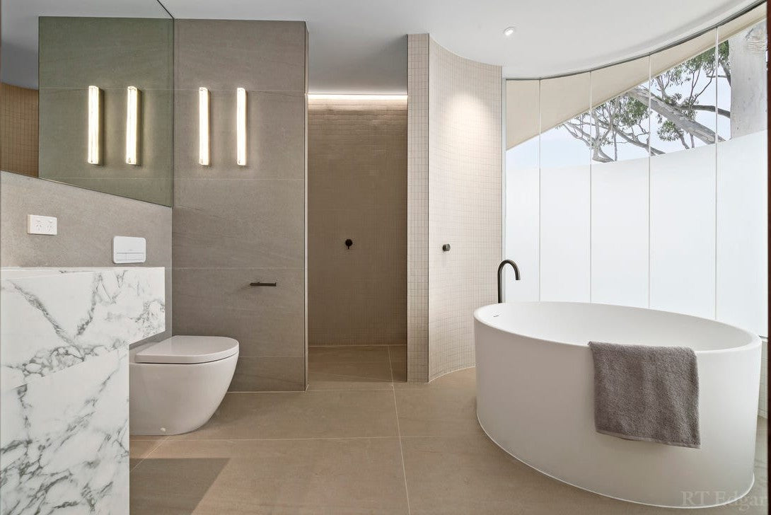 Ensuite with Running Water wall lamps and a freestanding bath beneath curved glass