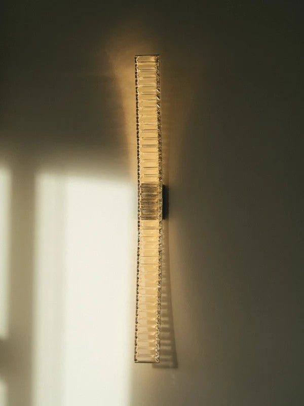 Pharaoh wall light lit on the living room wall, a slim curved blade of crystal