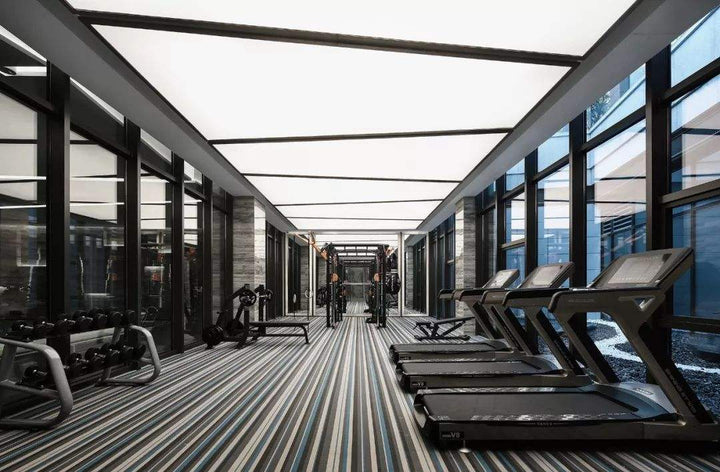 Ultra Panel Lighting LED stretch ceiling panels providing bright uniform illumination in a modern gym and fitness centre interior.